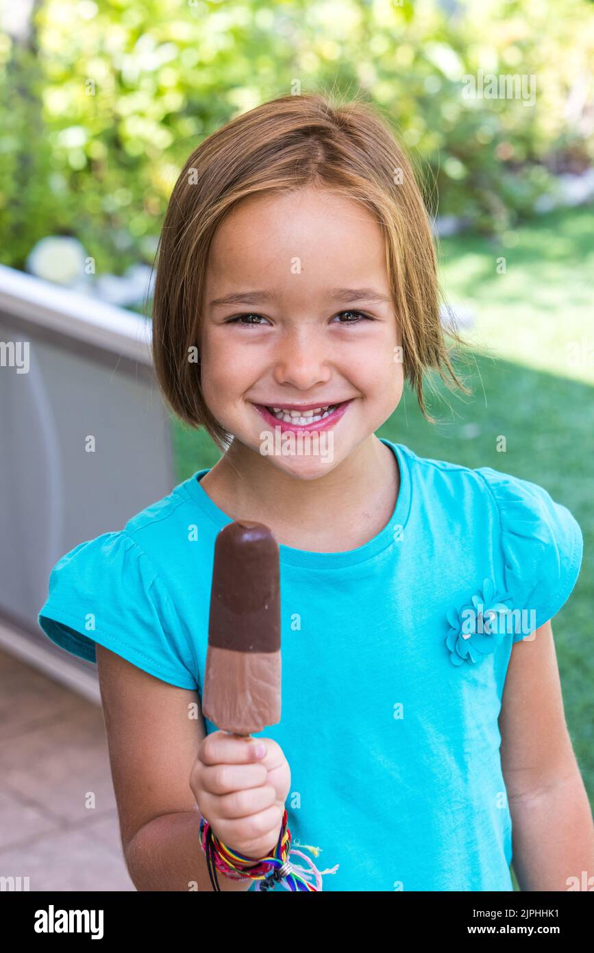 Girl wearing green tshirt, holding a milk chocolate ice cream, in the street, in summer