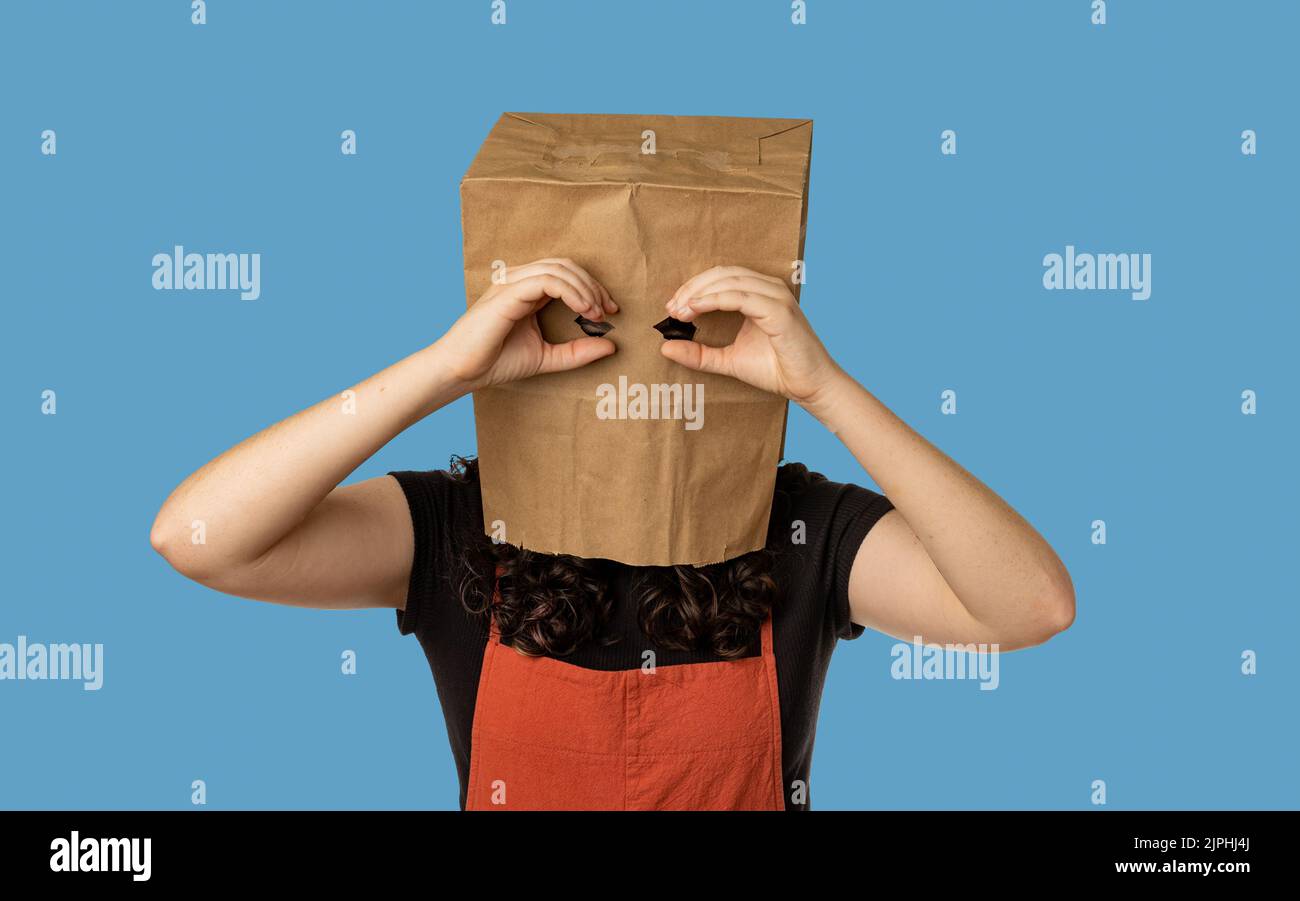 Woman wearing paper bag over her head holding her hands near eyes like binoculars Stock Photo