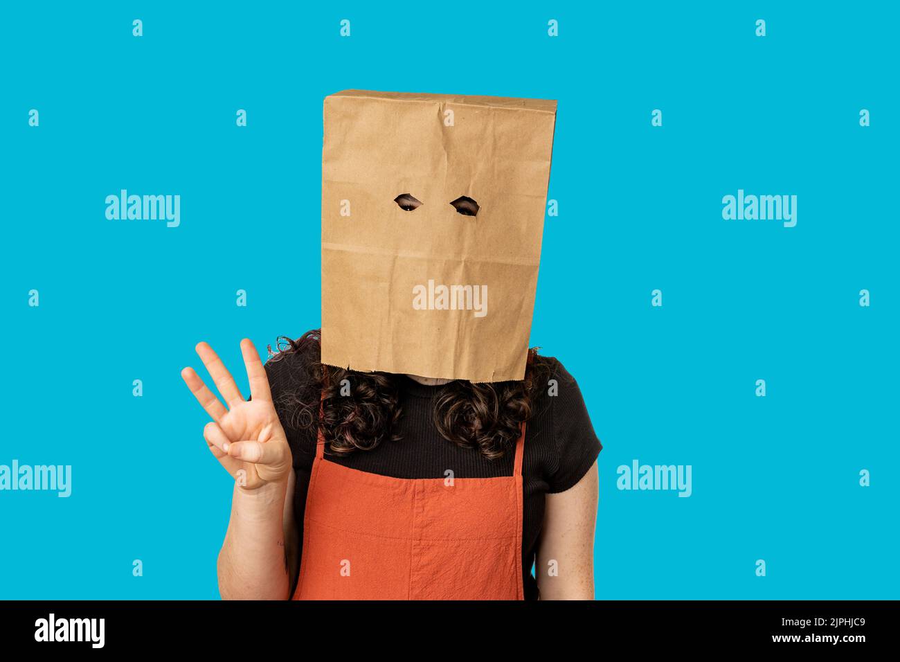 Woman wearing paper bag over her head holding up three fingers Stock Photo