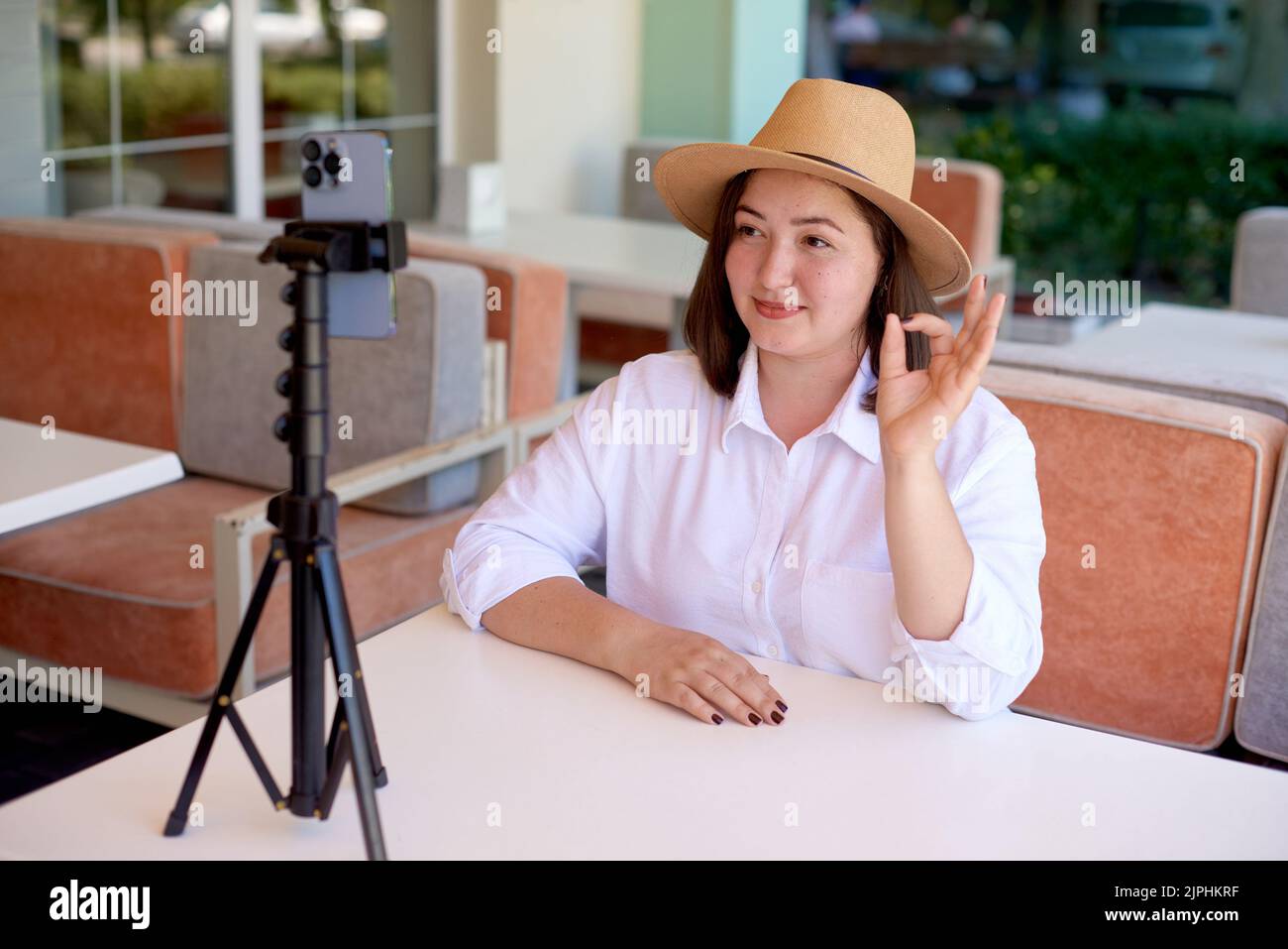 woman showing gesture all is well on phone camera. woman online with mobile phone on tripod streaming in summer terrace cafe Stock Photo