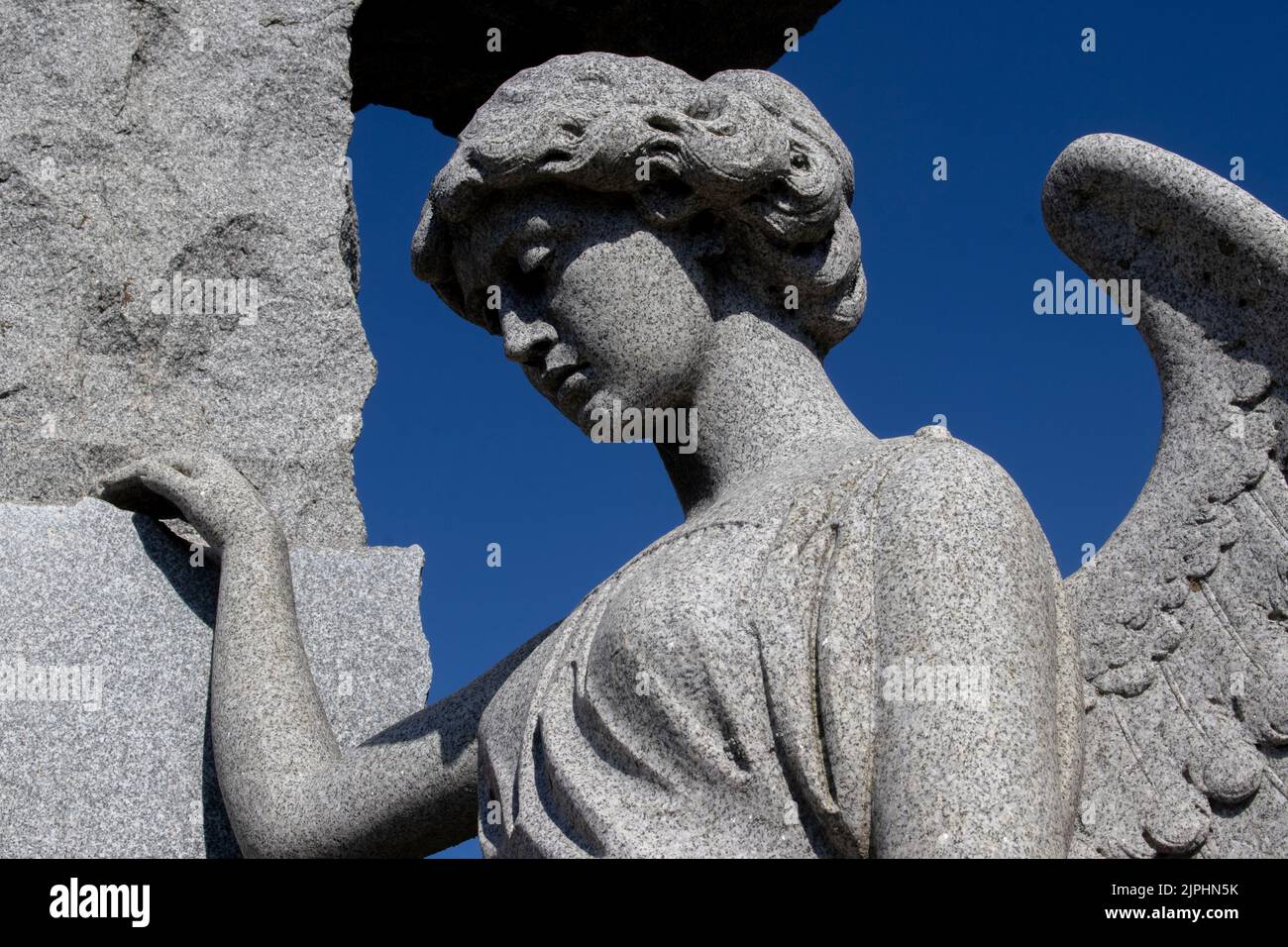 A stone angel stands with her hand on the cross and her wings partially