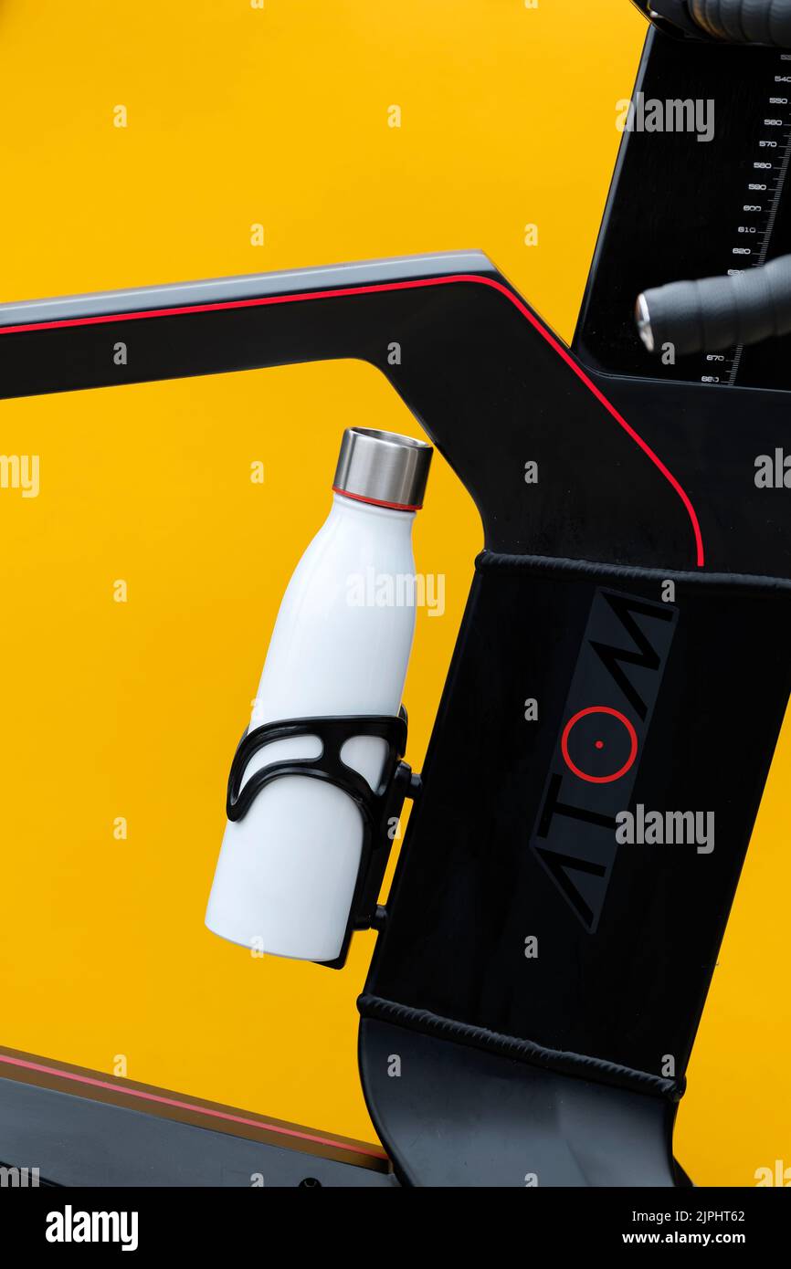 A metal screw top water bottle shown in the bottle cage of a Wattbike Atom. A smart bike indoor trainer. The image has a plain colourful background Stock Photo