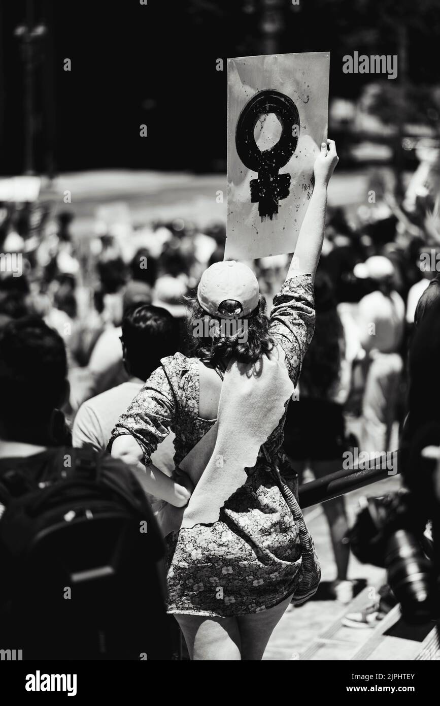 A vertical black and white shot of a woman at a protest holding a sign for women's rights Stock Photo