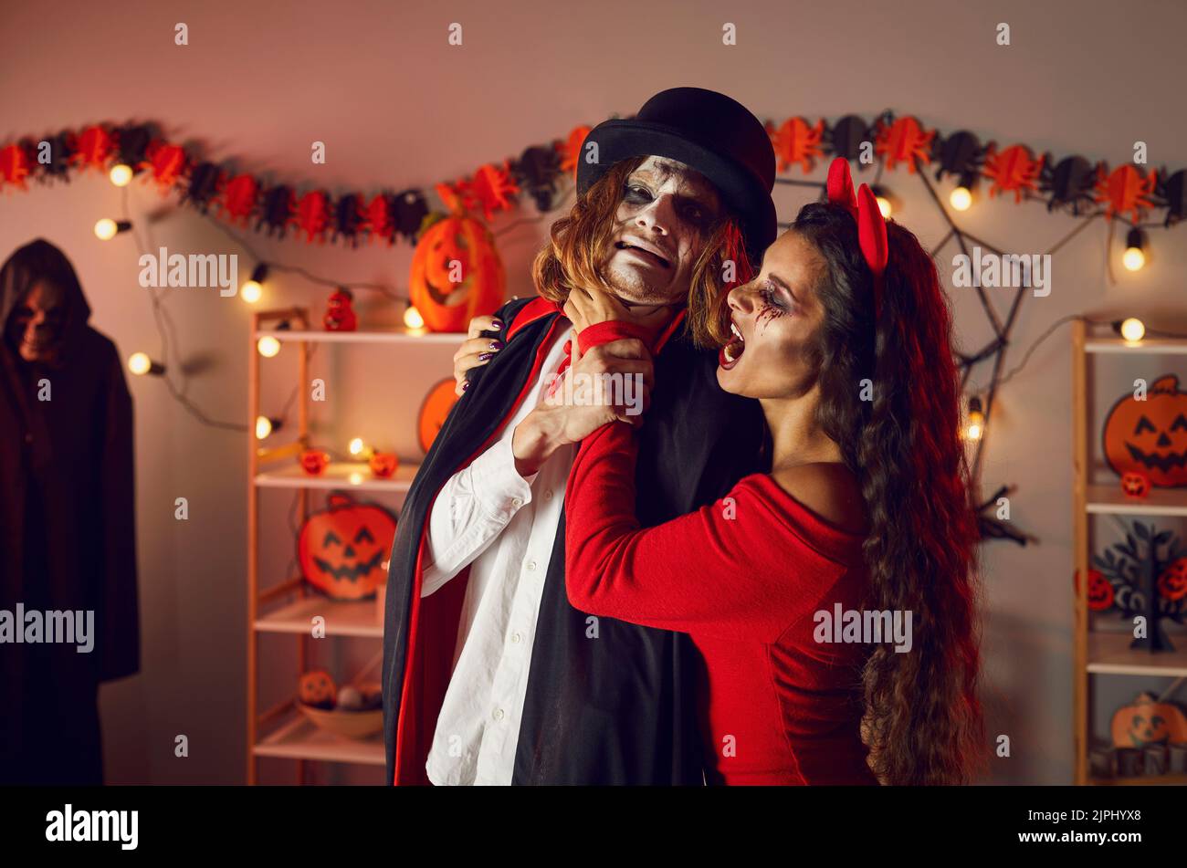 Devil woman having fun and jokingly choking scared vampire at spooky Halloween party Stock Photo