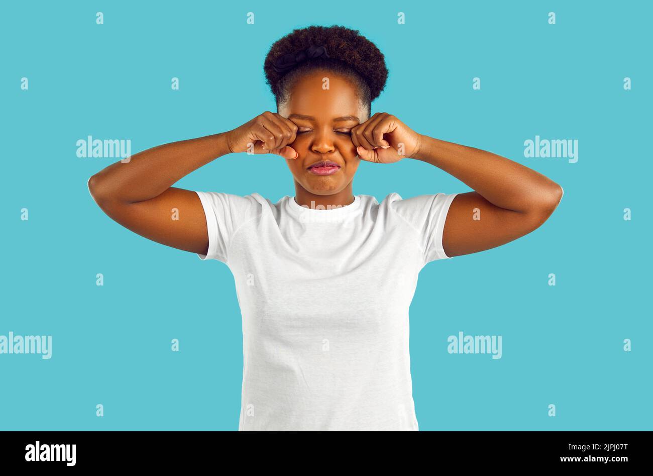 Funny capricious young african american woman pretending to cry against light blue background. Stock Photo