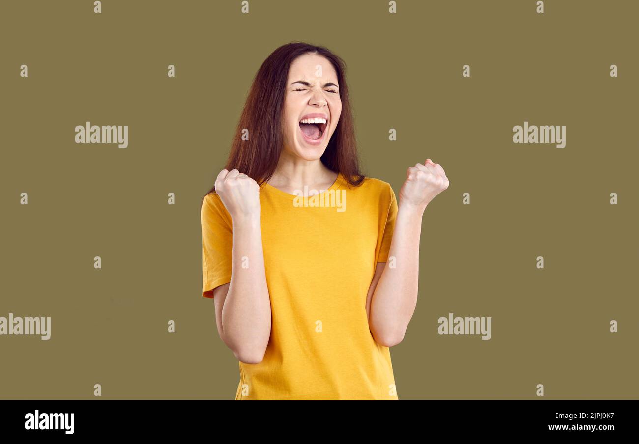 Happy crazy excited woman isolated on brown background clenching fists and screaming YES Stock Photo