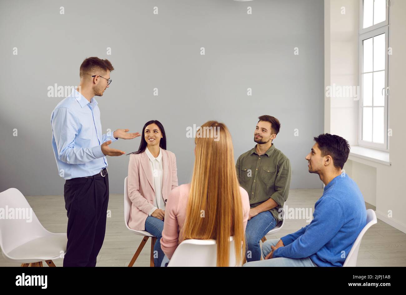 Young smart male coach or team leader speaks during work meeting or creative brainstorm. Stock Photo