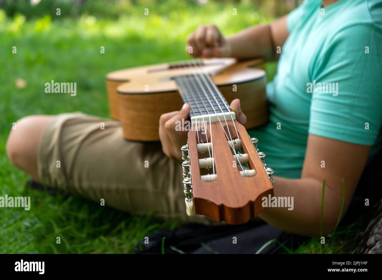 Boy with wooden guitar on green grass. Focus on the fretboard Stock Photo