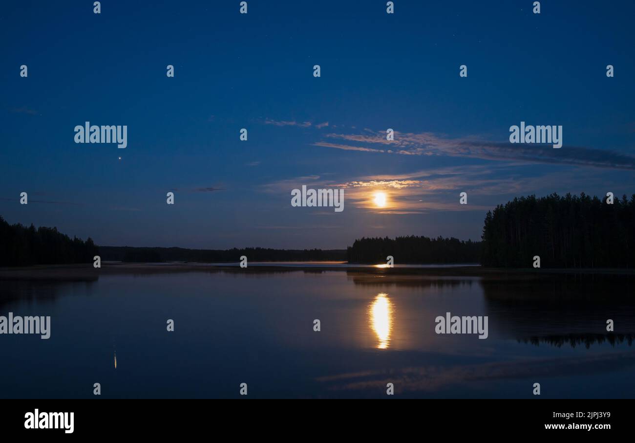 Moonlight night by the lake. Full moon and planet Jupiter in the sky and reflecting on water surface. Stock Photo