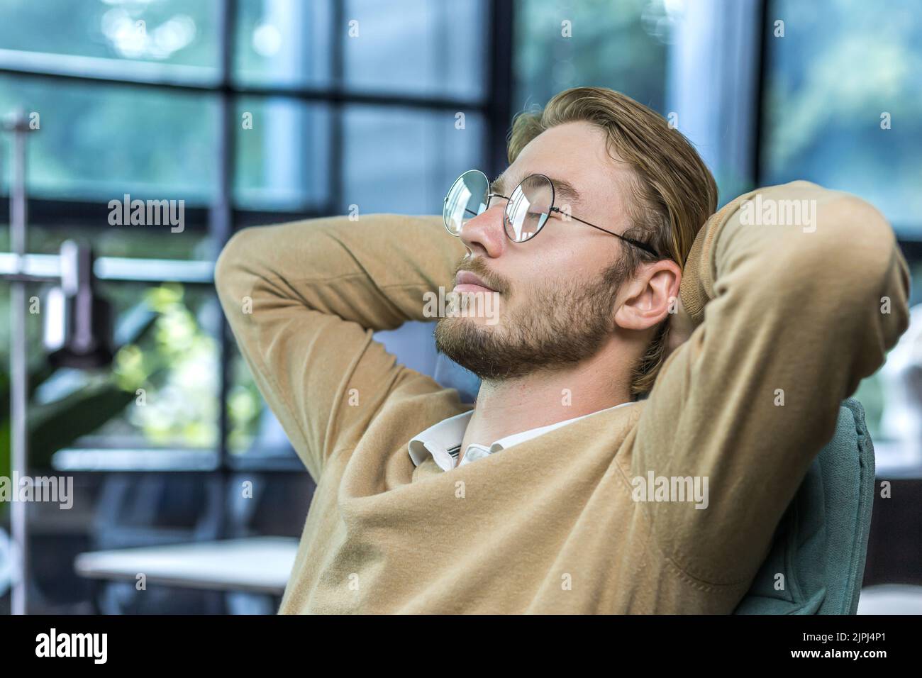 Man resting at home, young guy with closed eyes in glasses, hands behind head napping during the day, freelancer working at home remotely Stock Photo