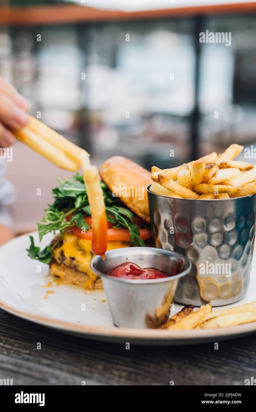 hand dipping French fries into ketchup at outdoor restaurant Stock
