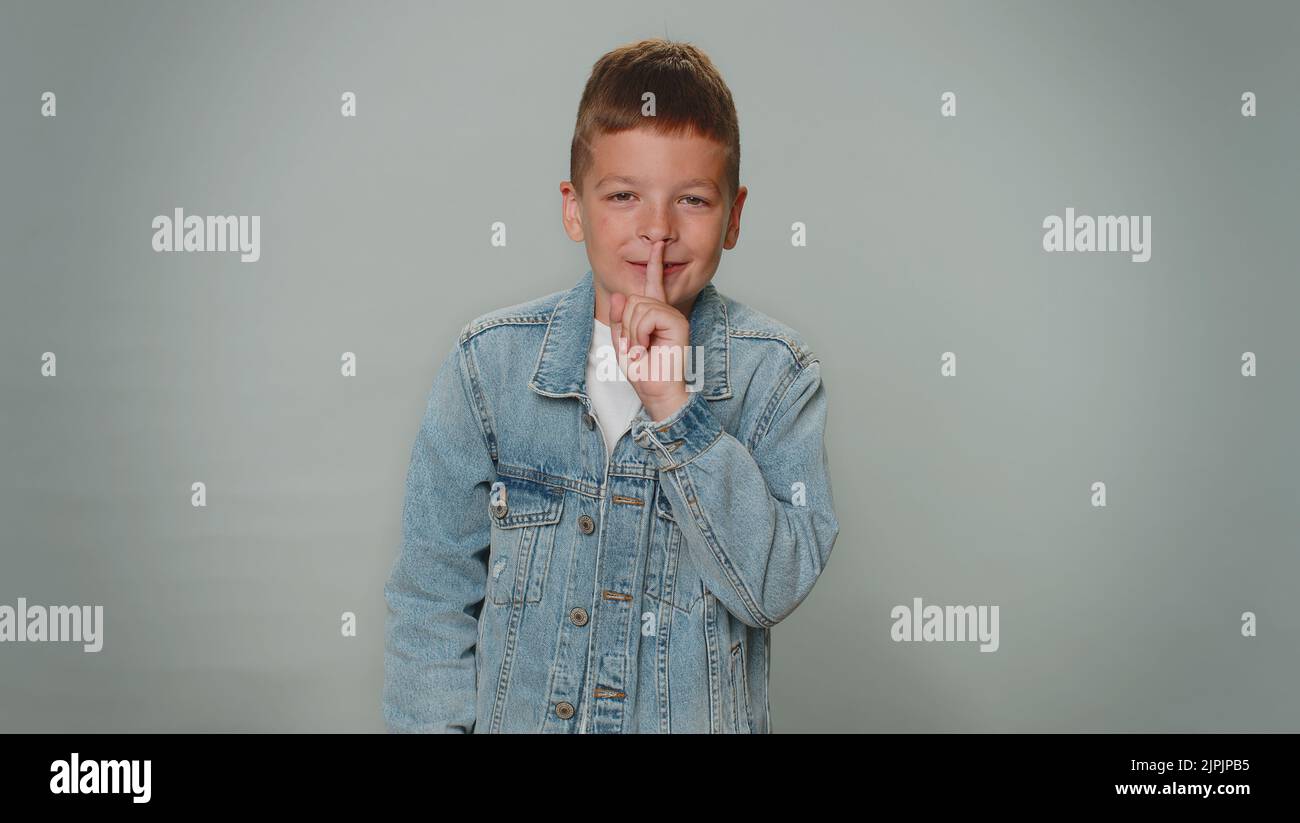 Shh be quiet please. Portrait of toddler boy 10 years old presses index finger to lips makes silence gesture sign do not tells secret. Young beautiful children teenager child on gray studio background Stock Photo