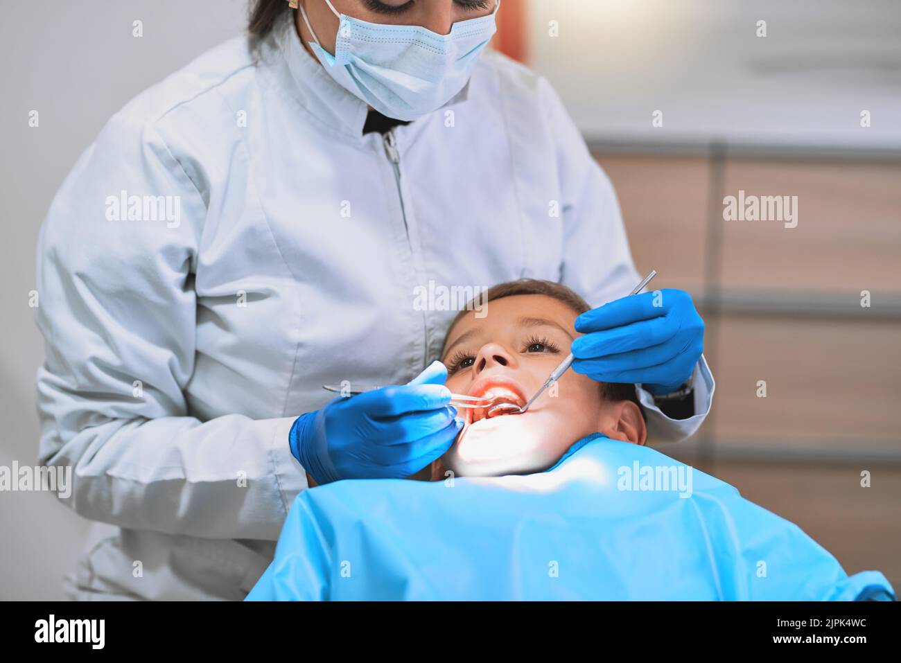 This is actually not too bad. a young little boy lying down on a dentist chair while getting a checkup from the dentist. Stock Photo