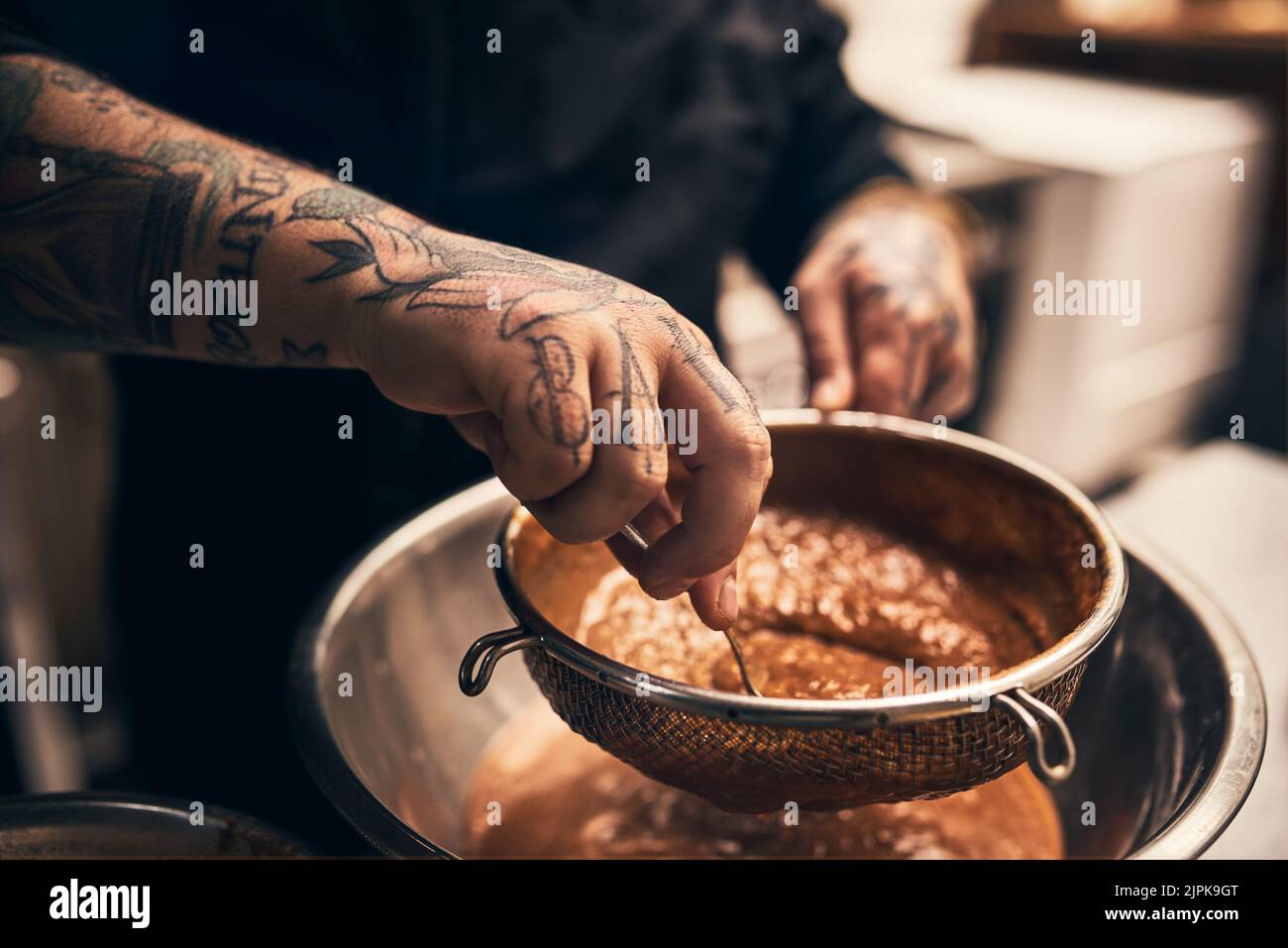 The best food is made with hard work. Closeup of a unrecognisable chefs tattooed hands straining food into a bowl in kitchen of a restaurant. Stock Photo