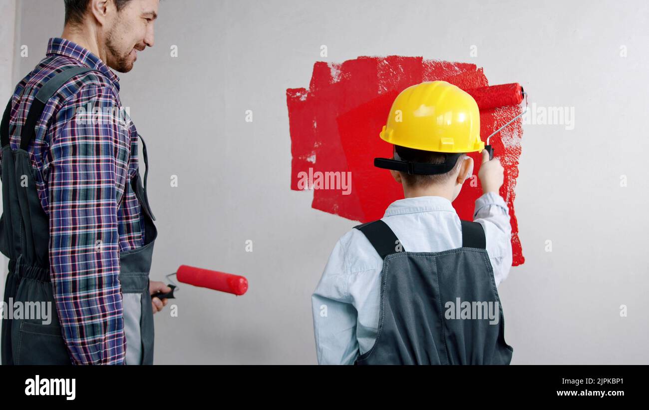 A little boy painting walls with red paint - his father watching him Stock Photo