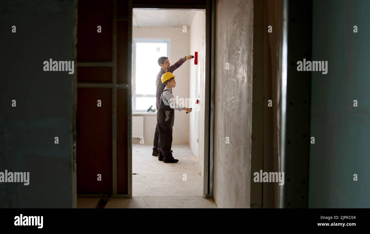 Repairing draft apartment - little boy and his father drawing lines on the wall with red paint Stock Photo