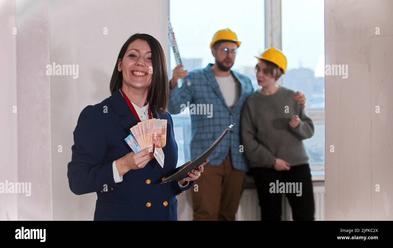 A real estate agent holding a lot of money in cash - young married couple looking around on the background Stock Photo