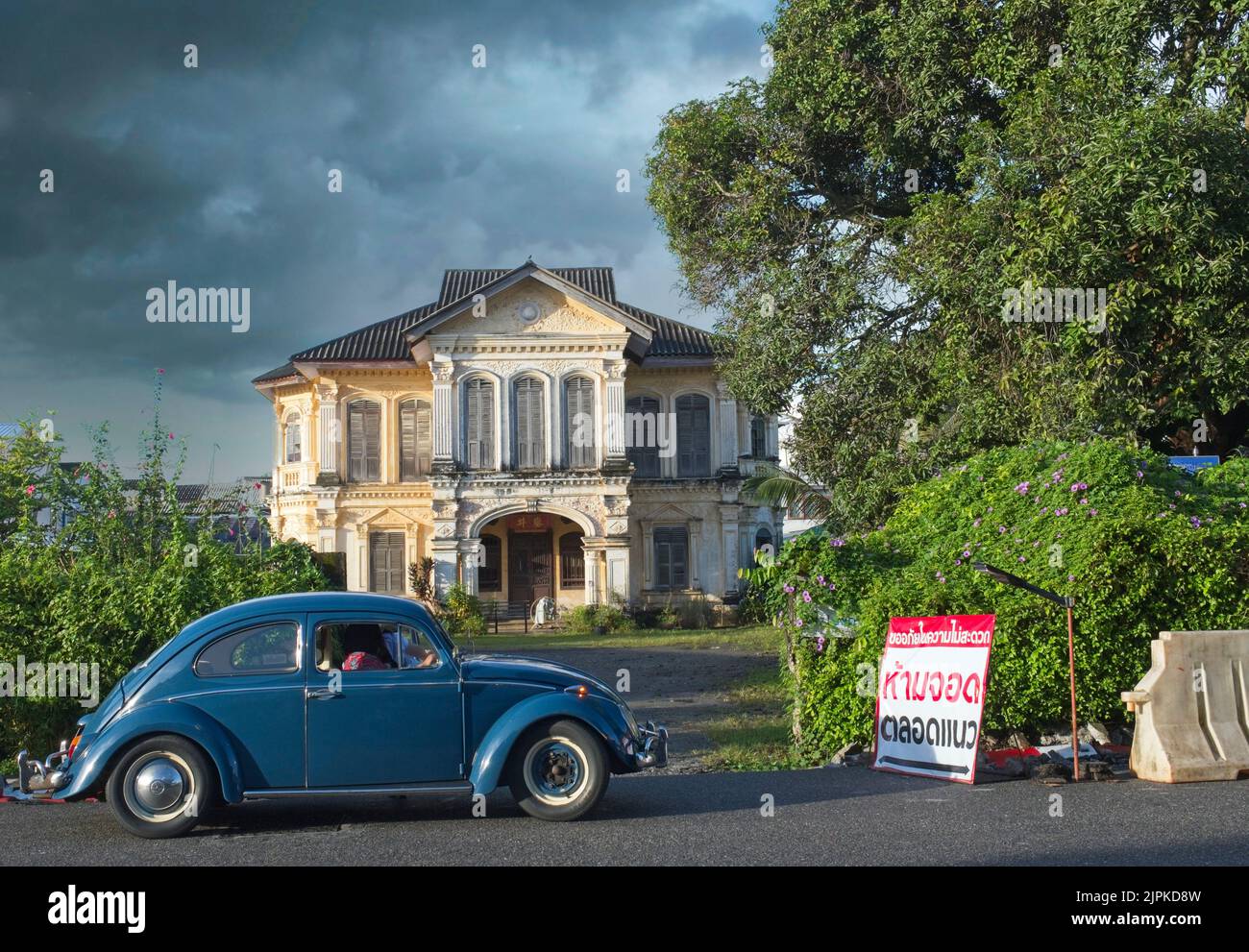 A VW Beetle stops at Luang Amnart Nararak Mansion, an old merchant's villa in the Old Town area of Phuket Town, Thailand, dark monsoon clouds looming Stock Photo