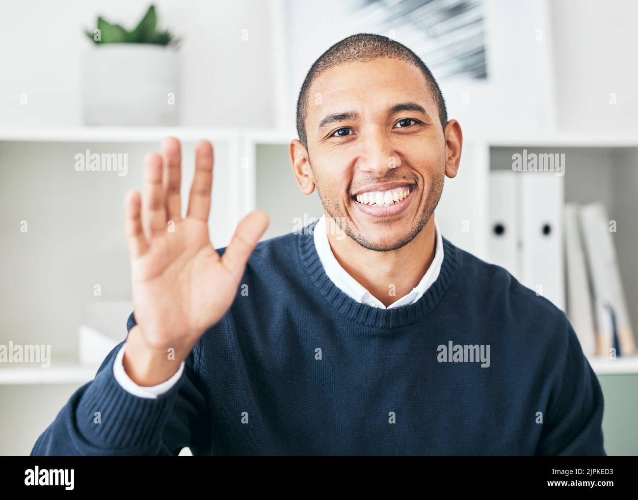 Waving, greeting and friendly employee with a bright smile and a positive mindset in the office. Portrait of a cheerful, joyful and excited Latino Stock Photo