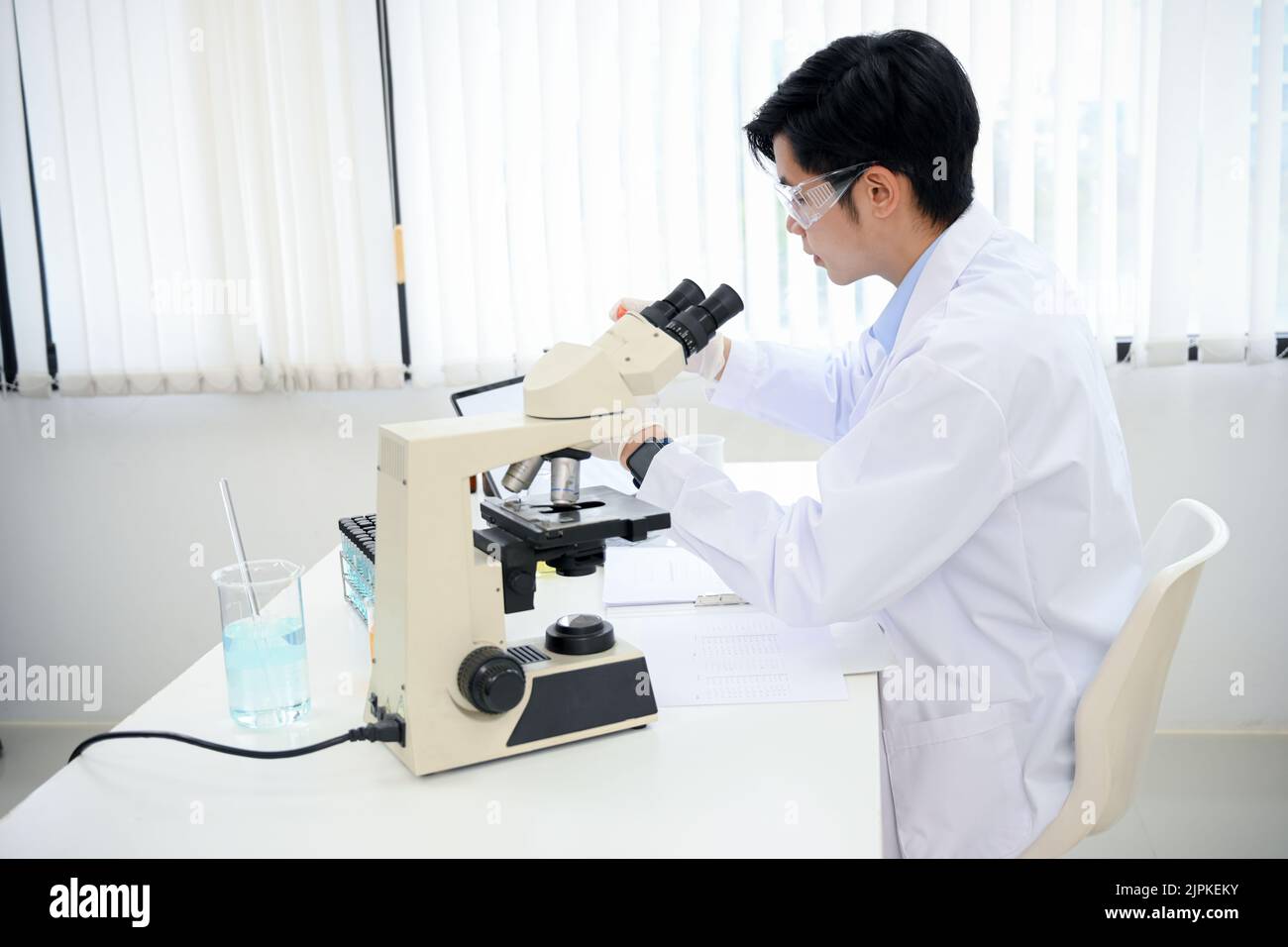 A handsome young Asian male scientist examining a virus specimen under