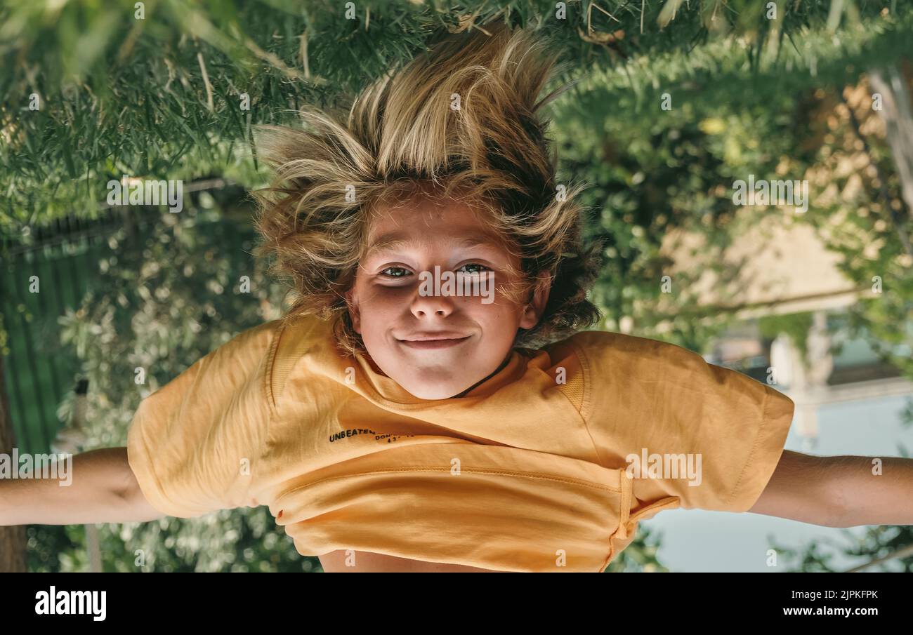 Kid hanging upside down while playing outdoors at backyard. Stock Photo