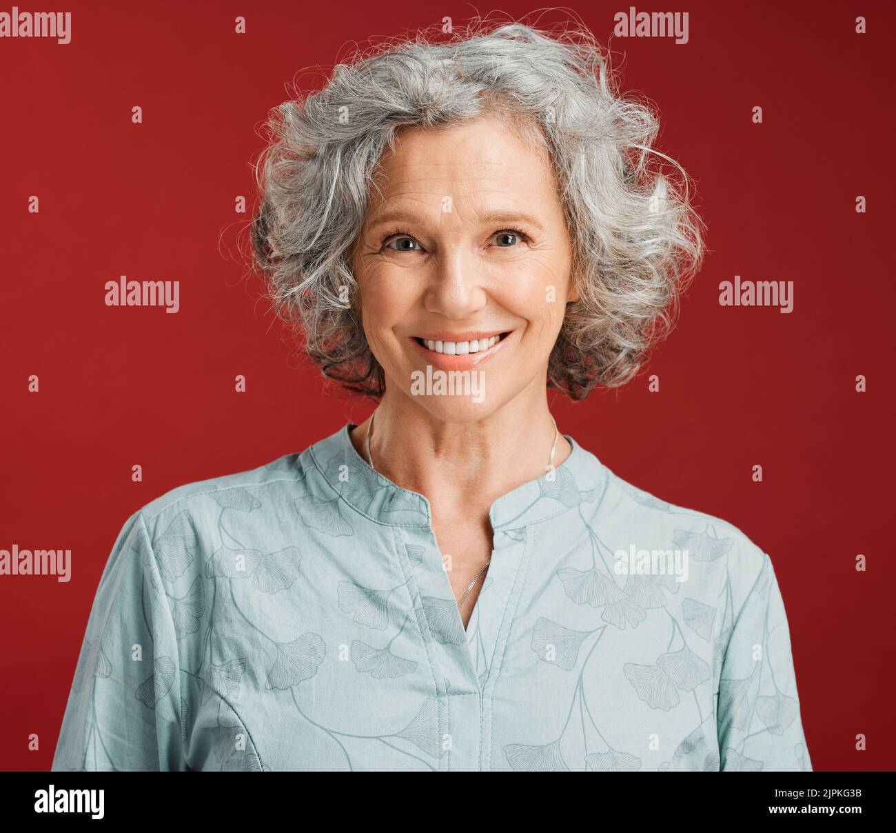 . Portrait of senior, happy and cheerful woman standing against a red studio background. Mature woman with healthy, white and clean teeth showing oral Stock Photo