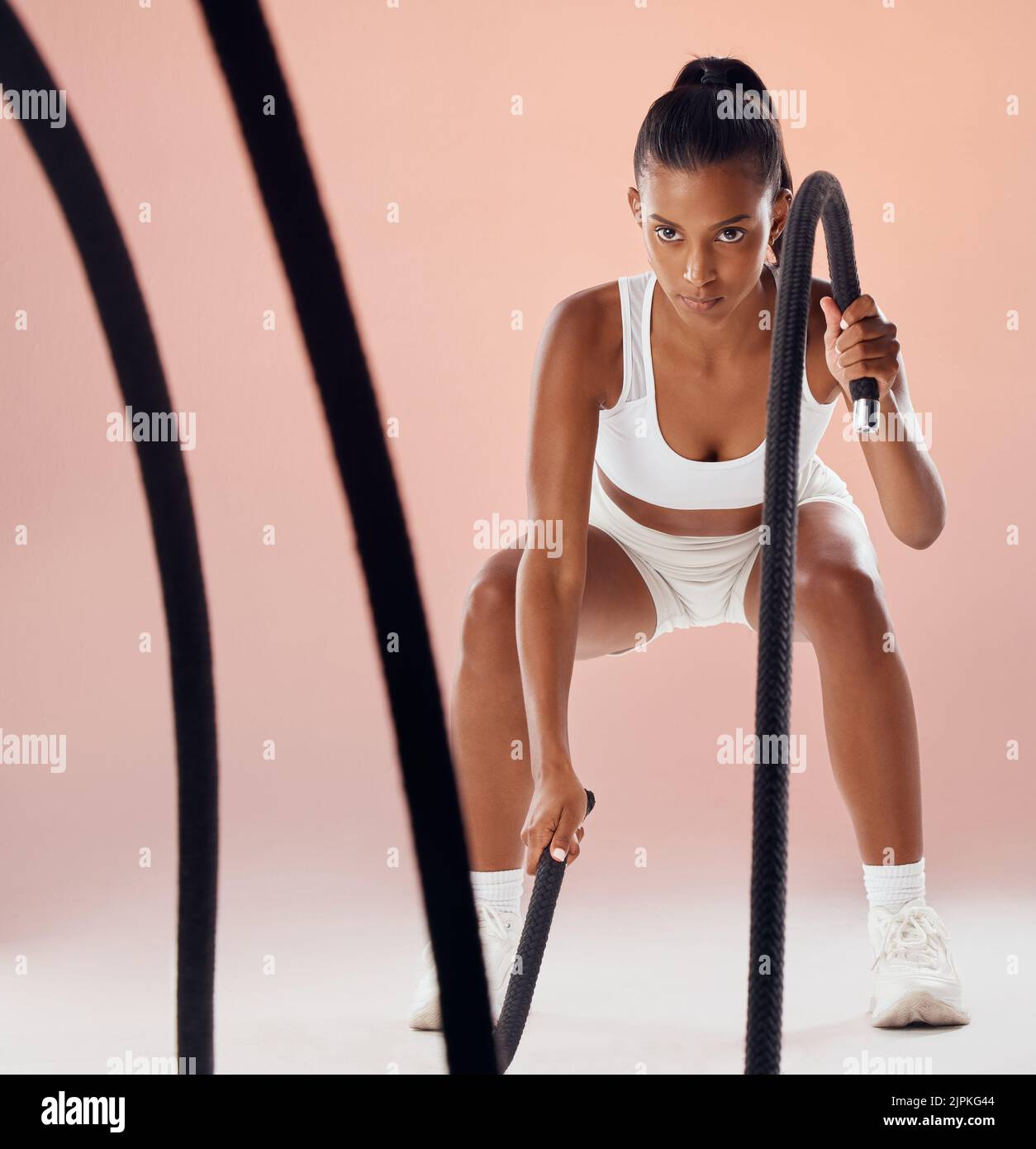 Fitness, battle ropes and active woman in a routine workout, training and exercise against pink studio background. Sporty, athletic and strong athlete Stock Photo