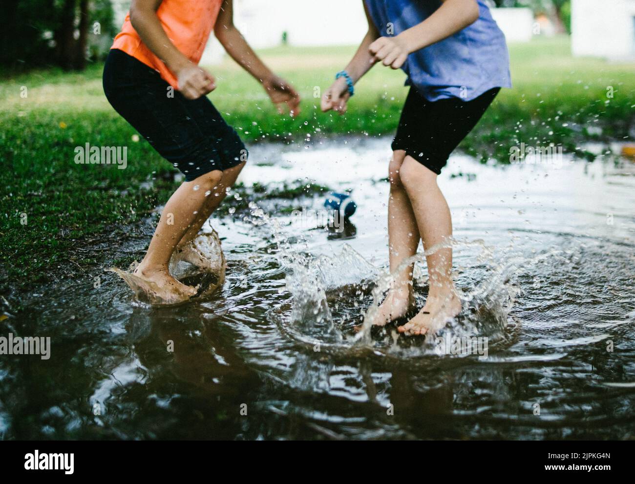 Two children jump into a rain puddle in green field Stock Photo Alamy