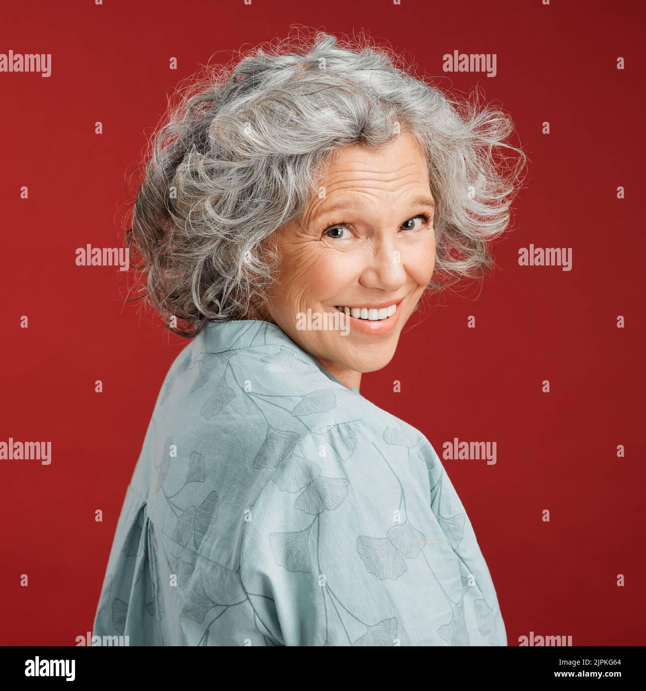 .. Confident, happy and smiling senior woman feeling playful and cheerful while posing against red studio background. Portrait of a beautiful, older Stock Photo