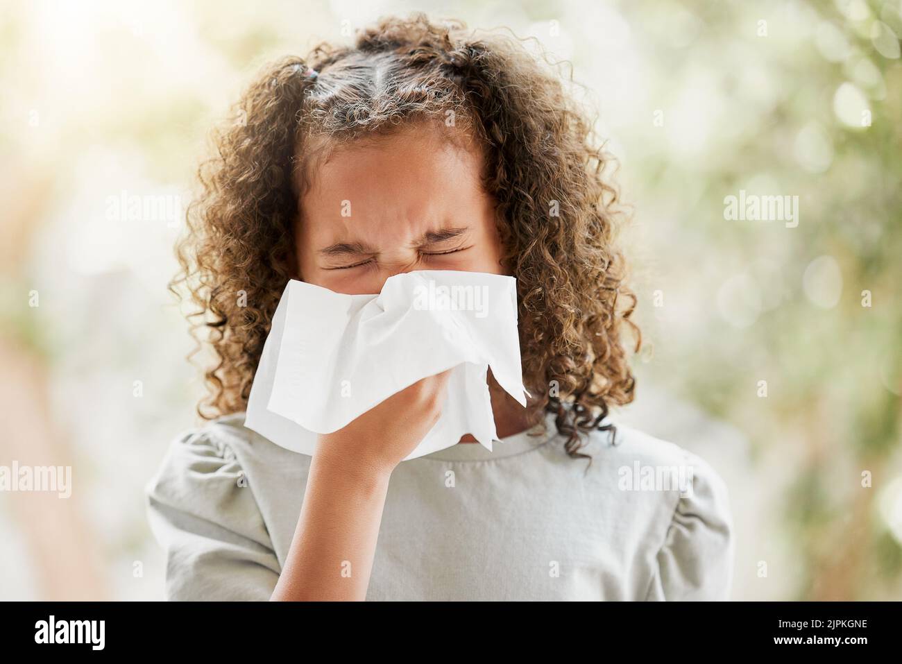 Sick little girl with a flu, blowing her nose and looking uncomfortable. Child suffering with sinus, allergies or covid symptoms and feeling unwell Stock Photo