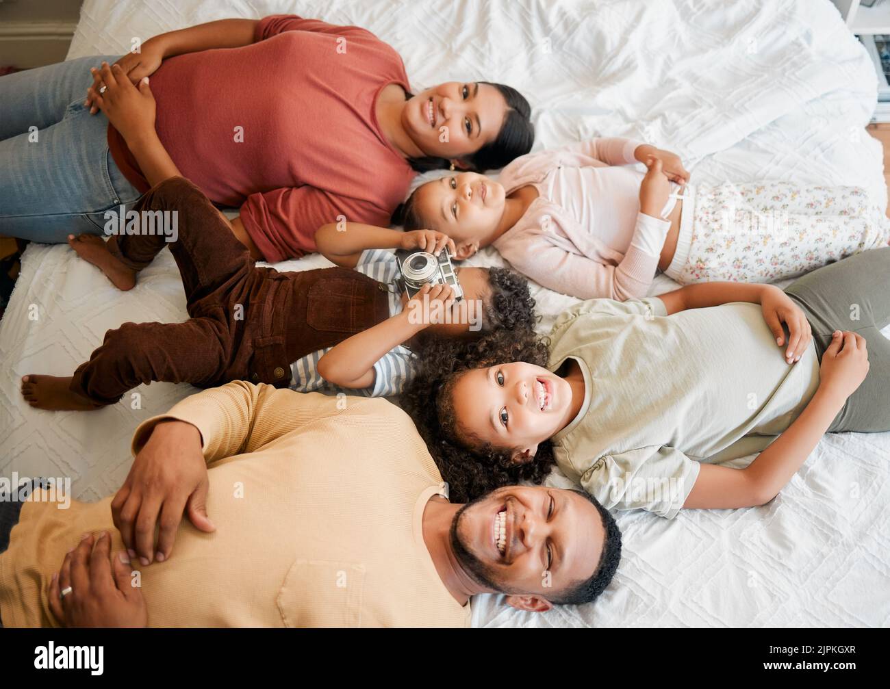 Fun family, children and parents bonding while lying on a bed in home bedroom from above. Portrait of playful, smiling and happy kids having fun with Stock Photo