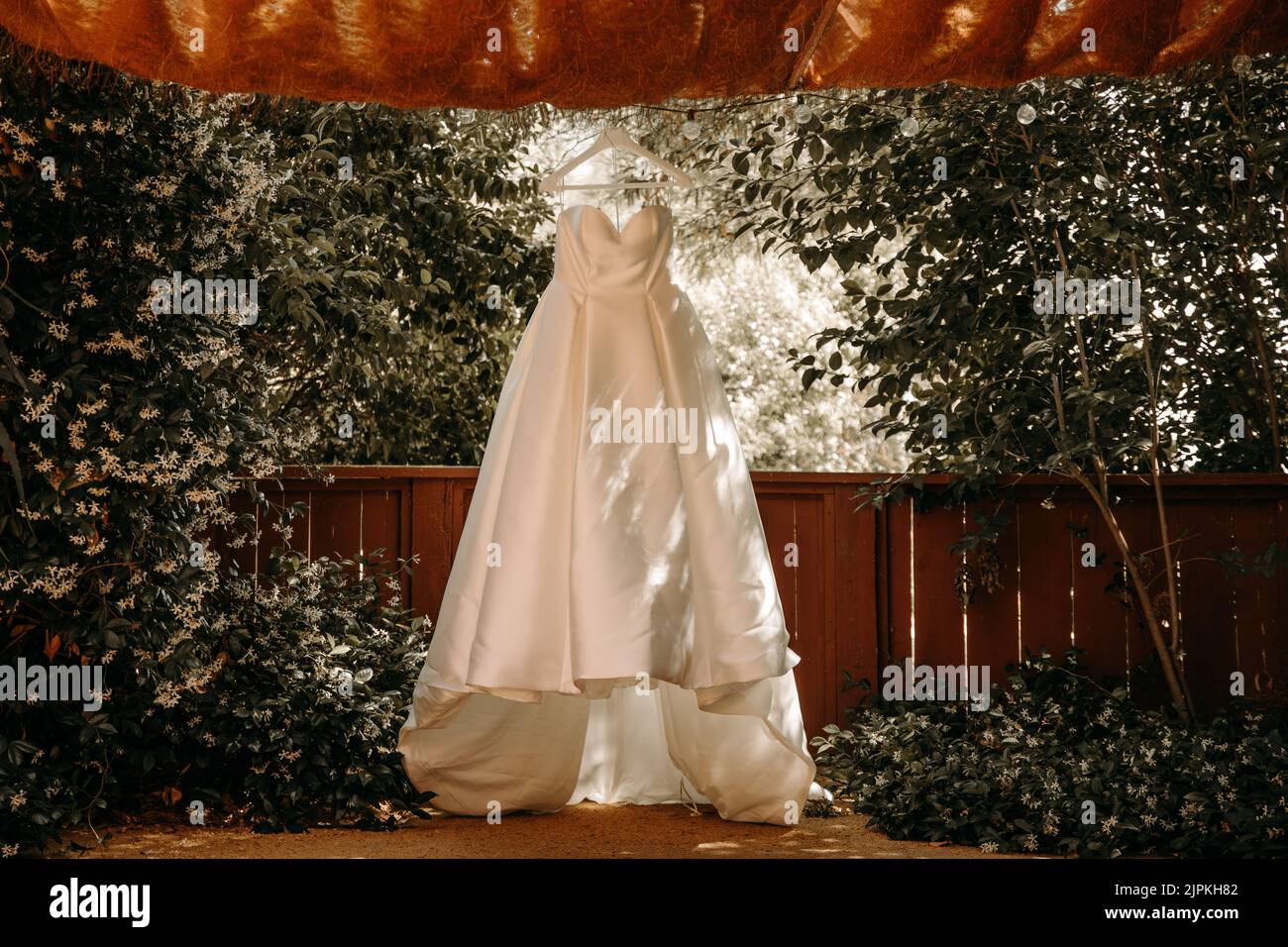 Beautiful wedding dress with pleats and tail hanging on white hanger outdoors. Ballgown in the garden. Stock Photo