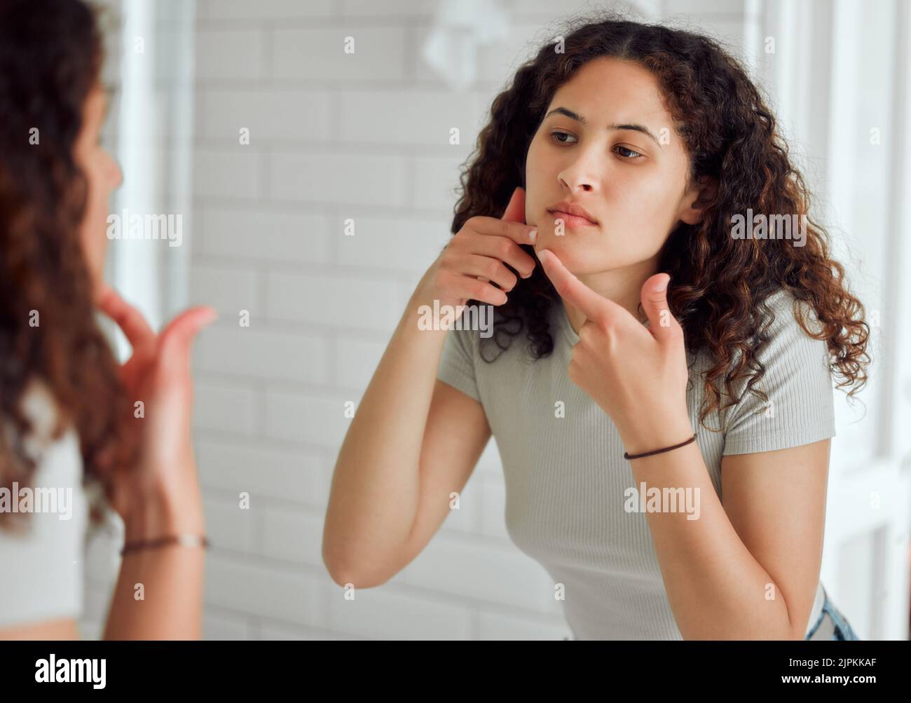 Woman popping a zit during a skincare routine while in front of a ...