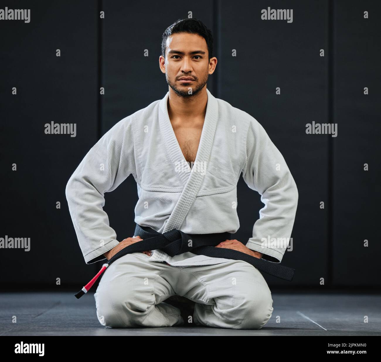 . Male coach ready for karate training at fitness studio, looking serious at dojo practice in gym and sitting on the floor at a self defense class Stock Photo