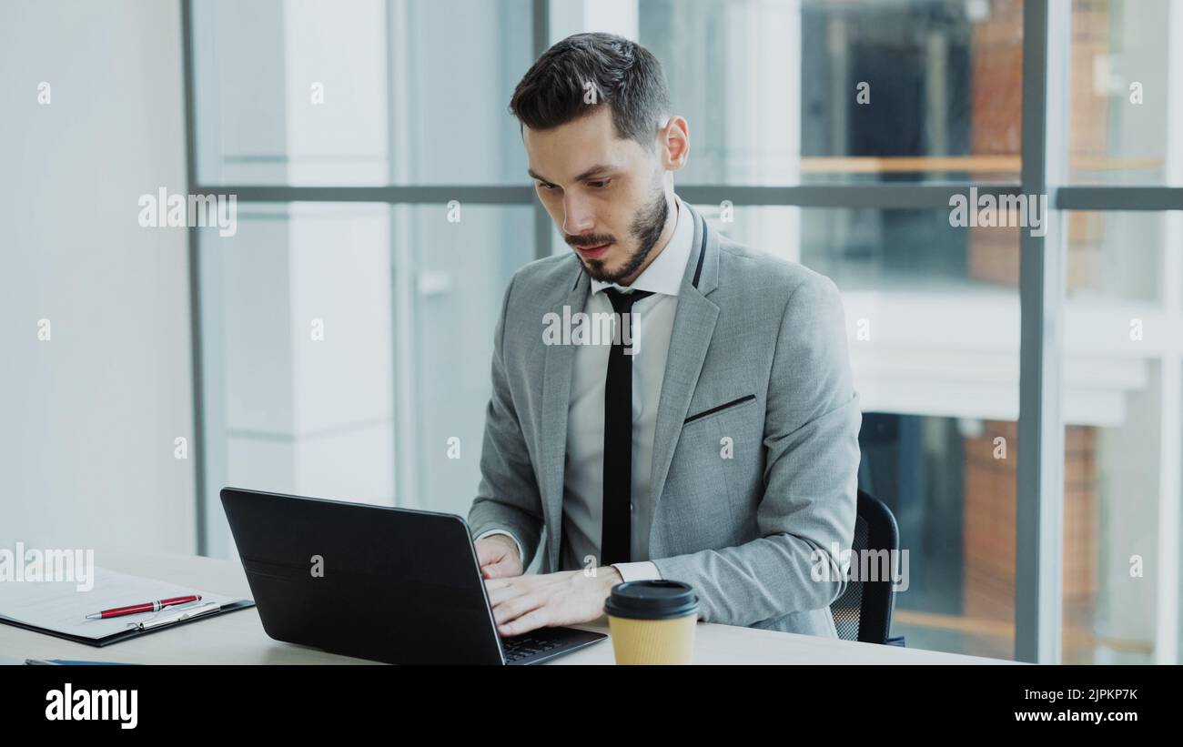 Young businessman using laptop computer sits in modern office indoors Stock Photo
