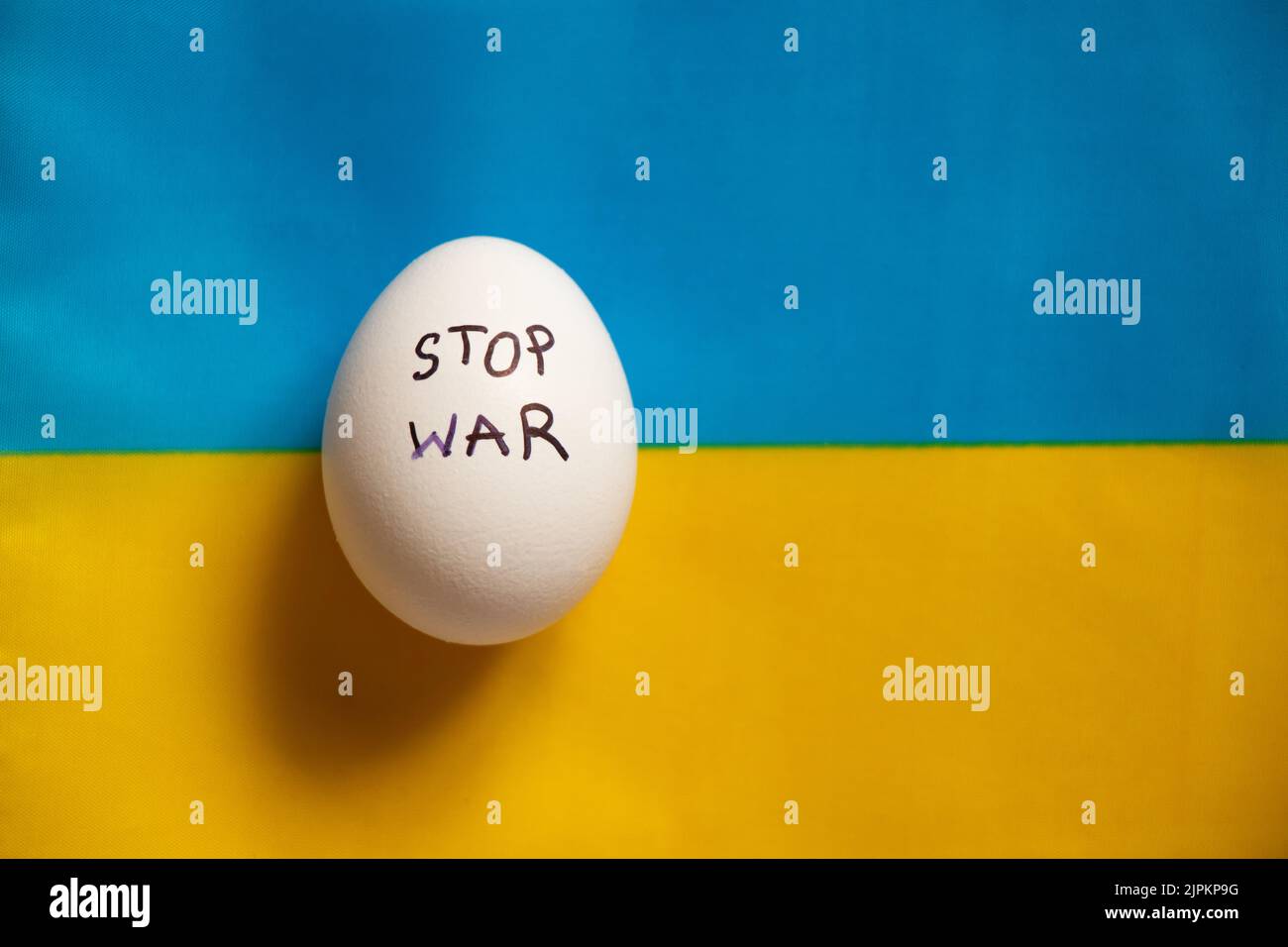 Stop war is written on a white chicken egg that lies on the yellow-blue flag of Ukraine, a protest action and support Stock Photo