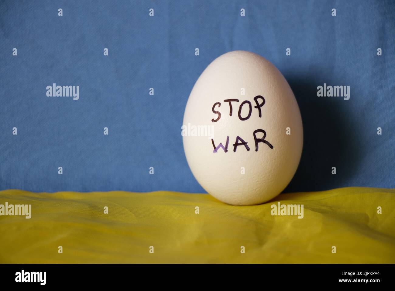 Stop war is written on a white chicken egg that lies on the yellow-blue flag of Ukraine, a protest action and support Stock Photo