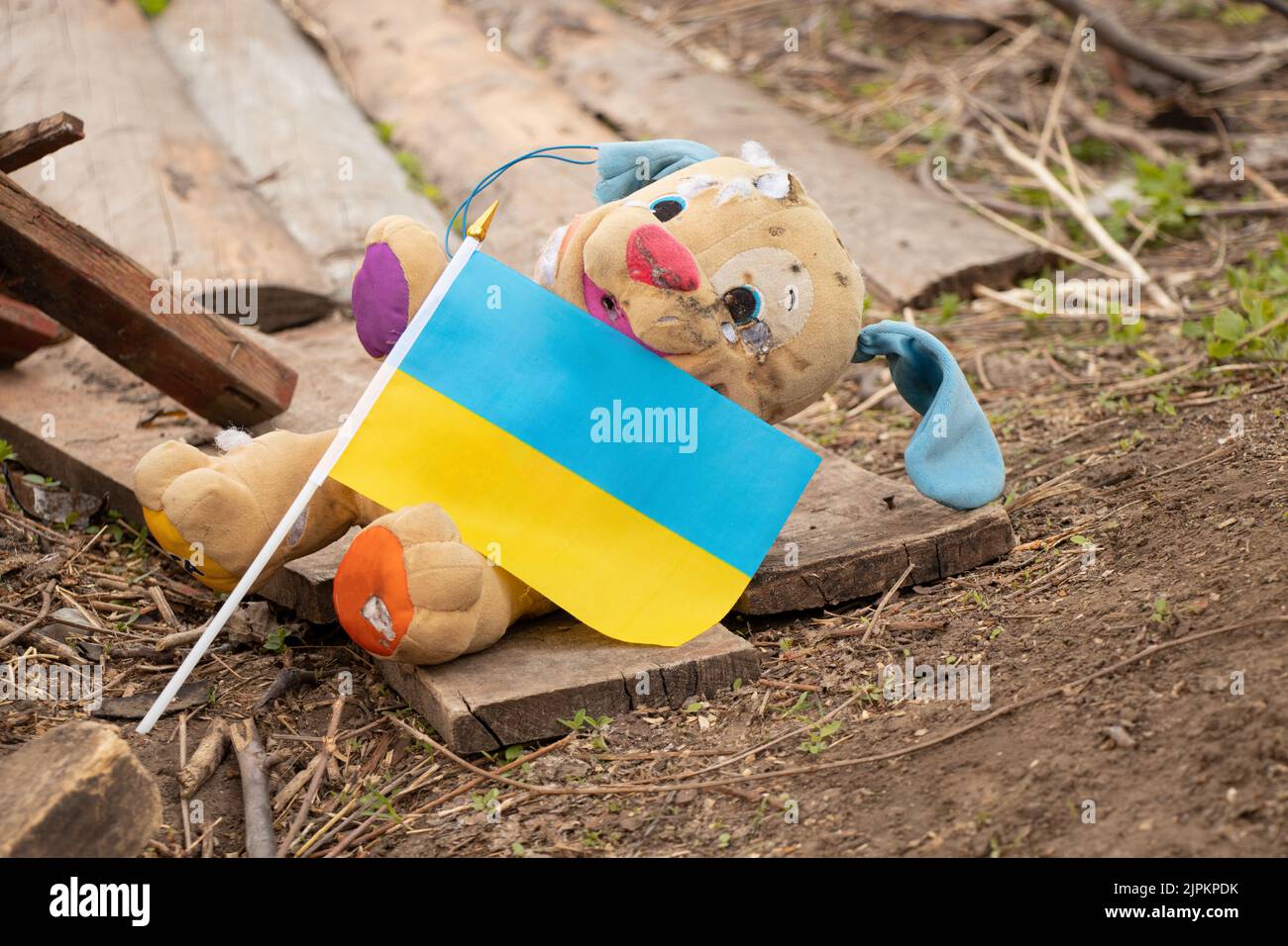 A dirty broken children's toy and the flag of Ukraine lies in the yard during the war in Ukraine, the death of children at the hands of Russian soldie Stock Photo