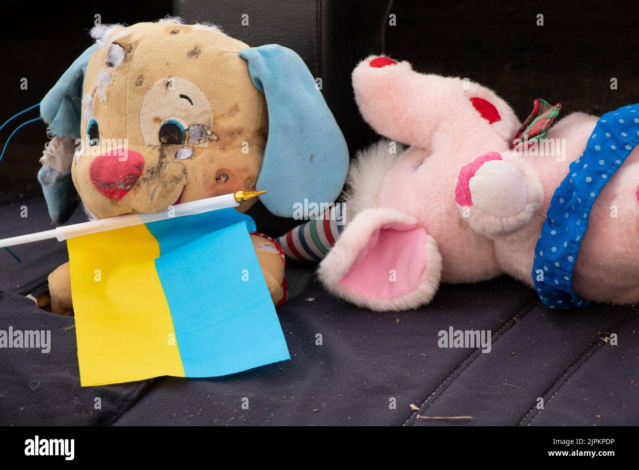 A dirty broken children's toy and the flag of Ukraine lies in the yard during the war in Ukraine, the death of children at the hands of Russian soldie Stock Photo