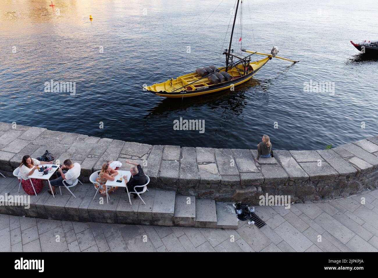 Overhead of people dining and chilling beside the Douro River in Porto's Ribeira aka Riverside district, Portugal. Sailing boat with wine barrels. Stock Photo