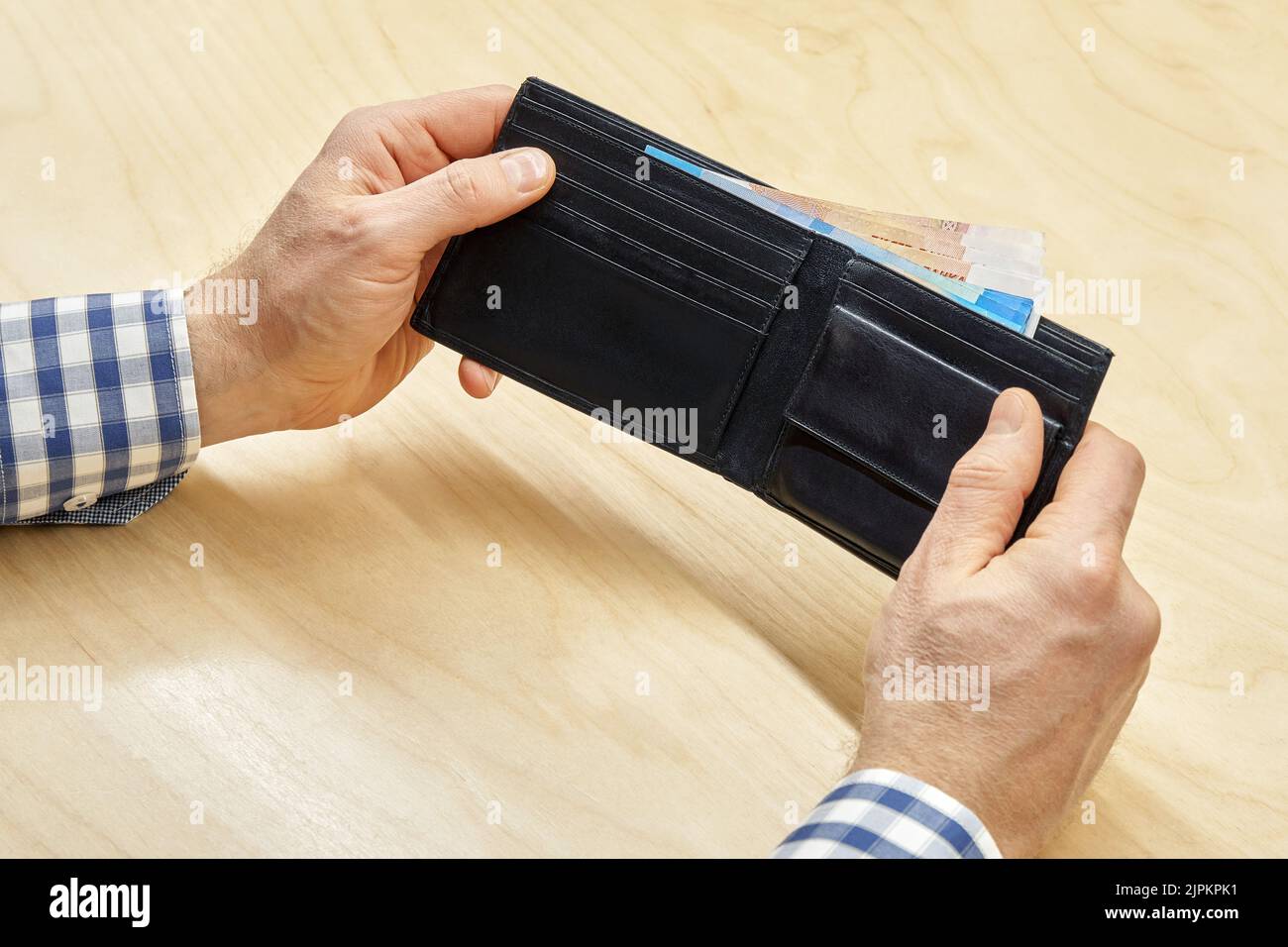 Man hands hold black wallet with money inside sitting at wooden table. Employee shows cash after getting salary. Employment and profit concept closeup Stock Photo