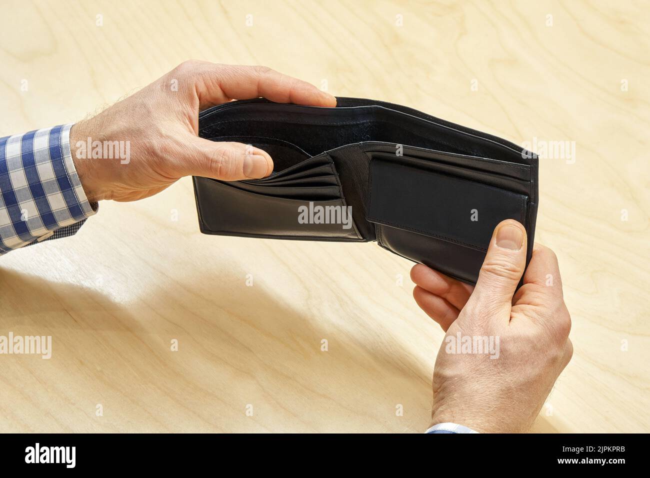 Hands of man hold empty black wallet against wooden table. Employee looks for money in purse. Poverty and crisis concept close view Stock Photo