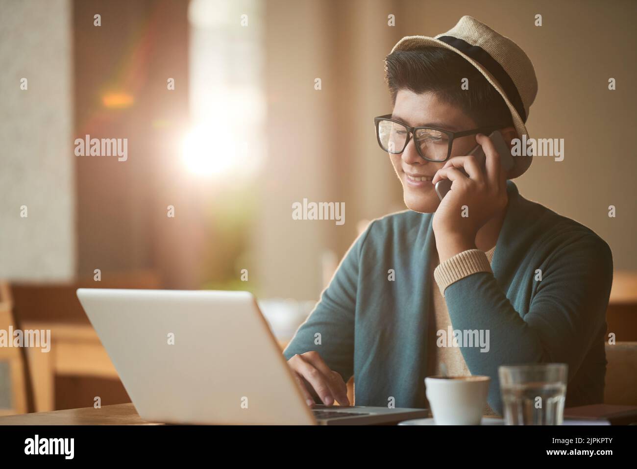 Smiling freelancer calling on phone when checking e-mails in his laptop Stock Photo