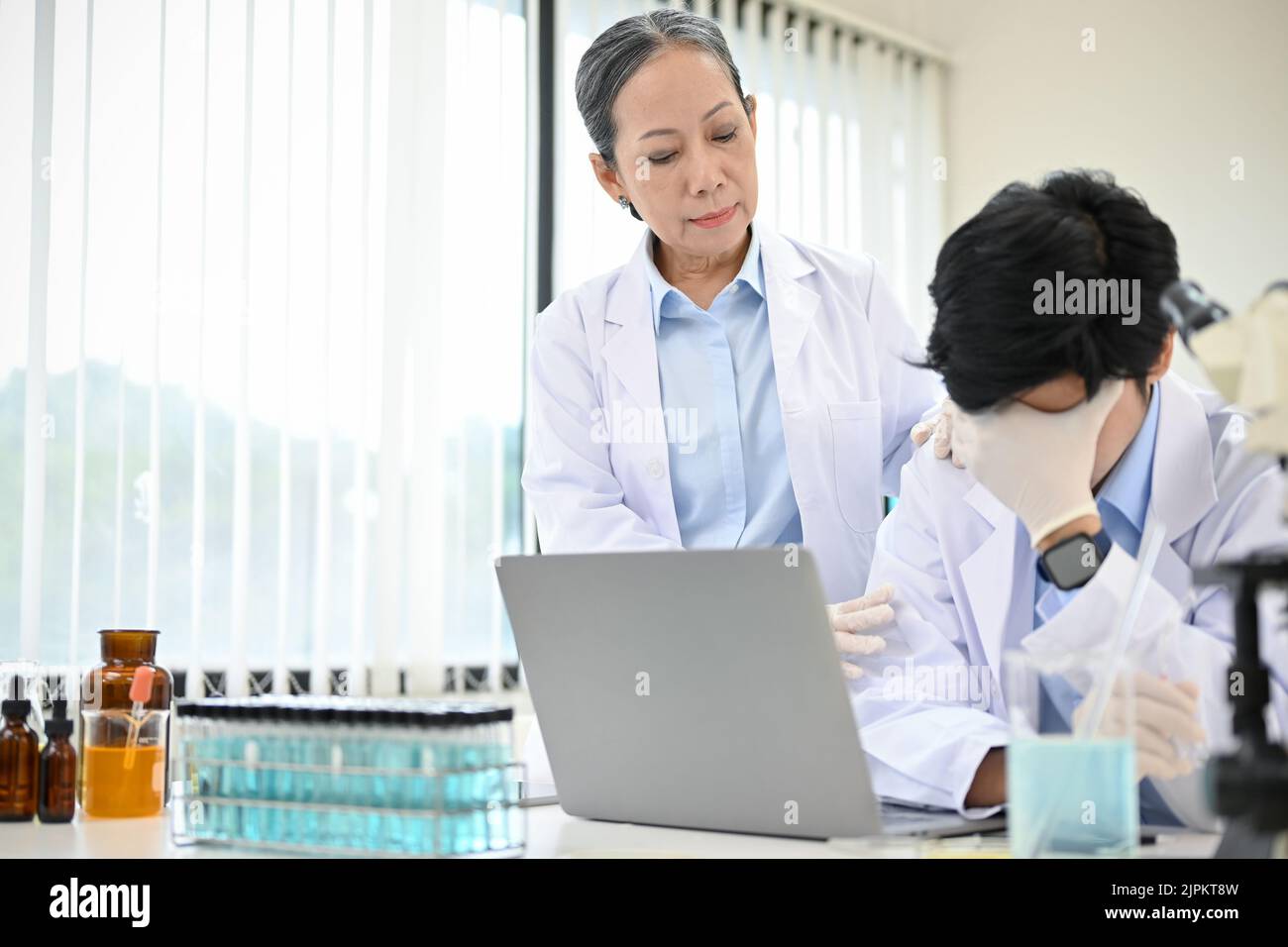 Stressed young Asian male scientist upset with his chemical experiment project while working in the lab with senior female professor. Stock Photo