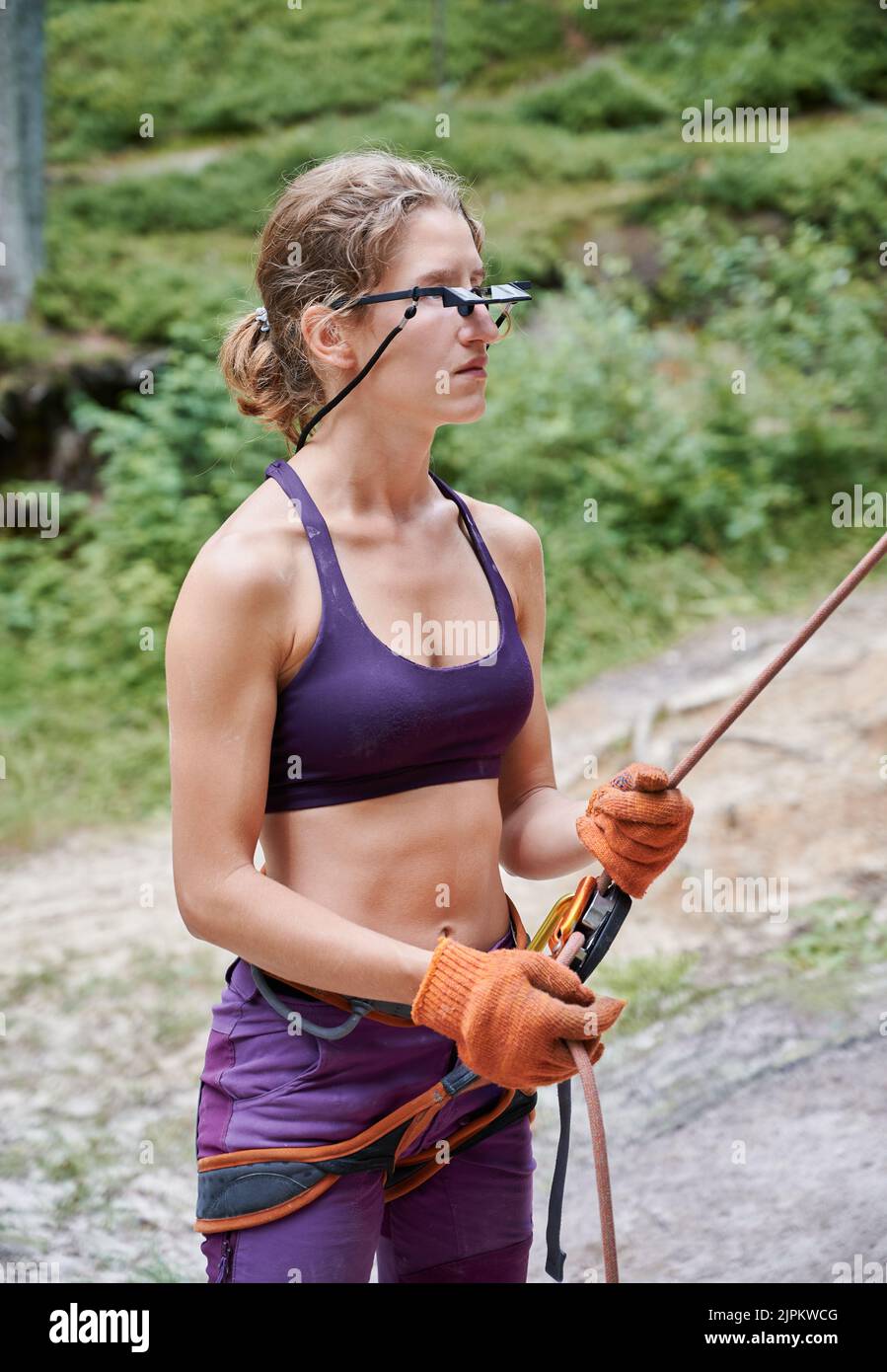 Female climber belaying leader during rock climbing outdoors, using rope, grigri, carabines. Young woman looking to his partner through glasses. Concept of extreme sport and outdoor activity. Stock Photo