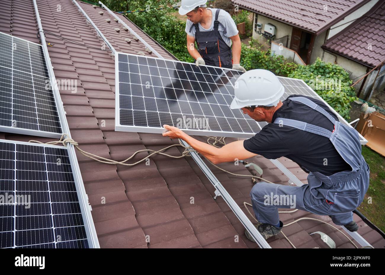 Men technicians carrying photovoltaic solar moduls on roof of house ...