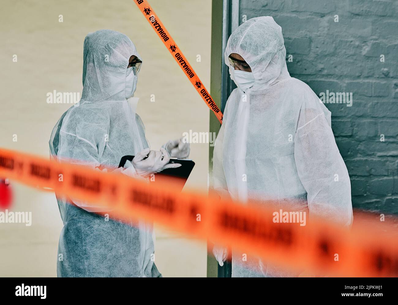 Forensic investigators collecting evidence at a murder scene in a building with barrier tape. Criminal researchers investigating a crime site and Stock Photo