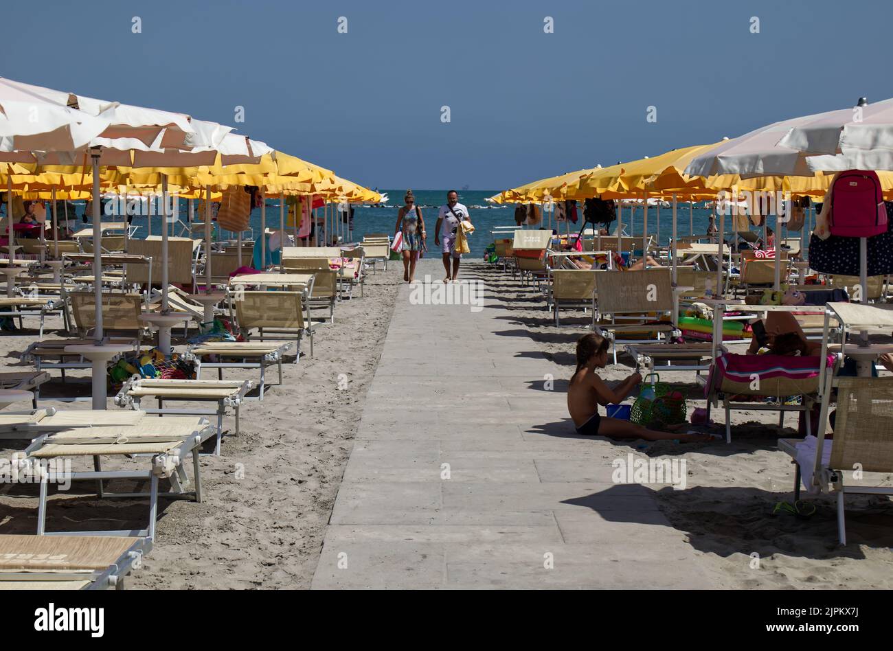 Italian beach view with umbrellas and sunbeds. White walking path