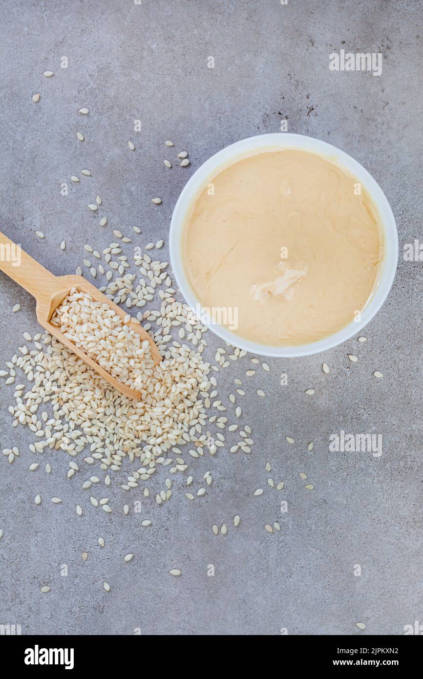 Pure sesame tahini with sesame seeds on mottled grey with copy space