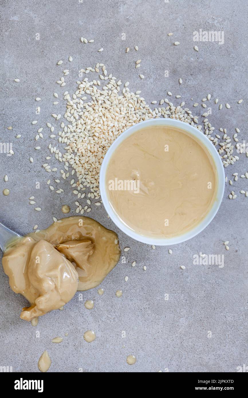 Pure sesame tahini with sesame seeds on mottled grey with copy space